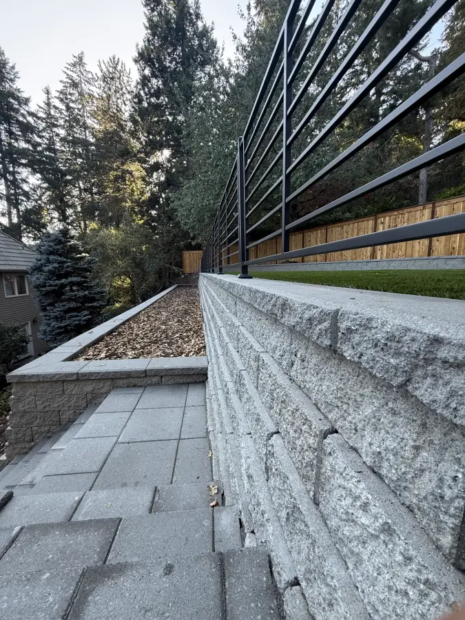 Split-face engineered retaining wall, stone stairway, and custom steel railing system by Rubi Construction LLC